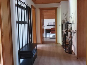 A hallway with a black metal rack, a wooden bench, and a shelf with decorative branches and flowers.
