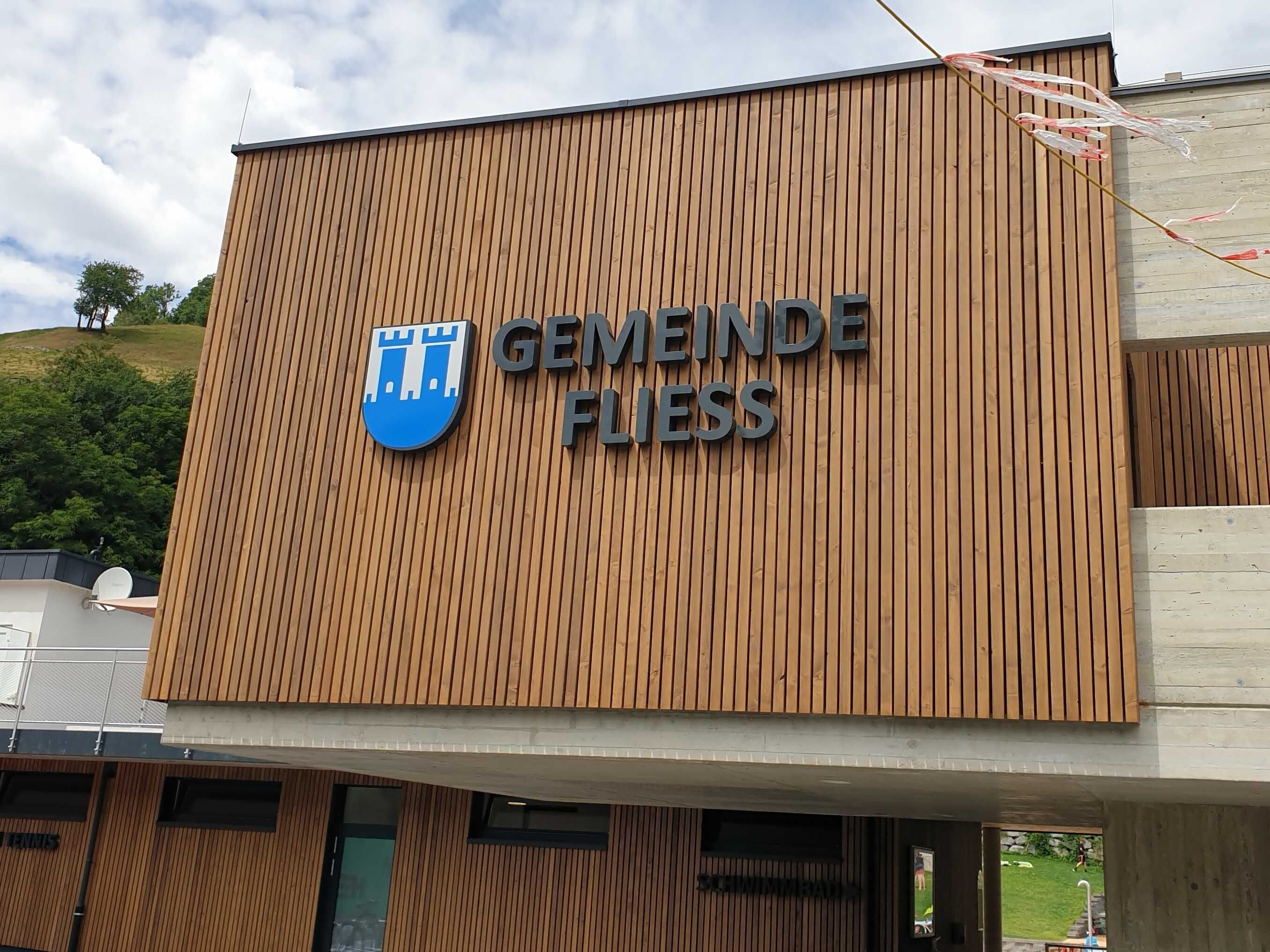 Un bâtiment sur lequel on peut lire l’inscription « GEMEINDE FLESS » et qui arbore un logo représentant un château.
