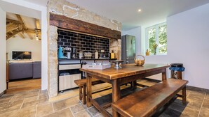 A kitchen with a stone wall, wooden beams, and a tiled floor. - Villa les Rocs (La Bachellerie)
