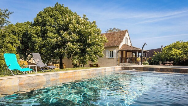 A clear swimming pool with lounge chairs, a gazebo, and a building with a tiled roof. - Villa les Rocs (La Bachellerie)