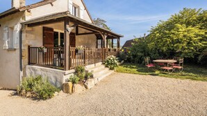 A two-story house with a covered porch, a gravel driveway, and a garden with a table and chairs. - Villa les Rocs (La Bachellerie)