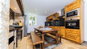 A compact kitchen with wooden cabinets, a built-in oven, and a dining area with a bench. - Villa les Rocs (La Bachellerie)