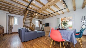 A spacious living area with a wooden ceiling, a grey sofa, a dining table with chairs, and a staircase. - Villa les Rocs (La Bachellerie)