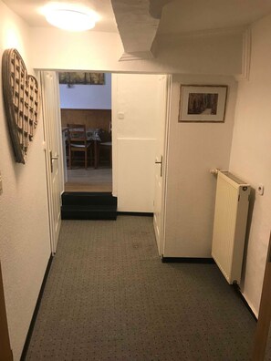 Ein Flur mit einer Tür zu einem Zimmer, einem Heizkörper und einem gerahmten Bild an der Wand.