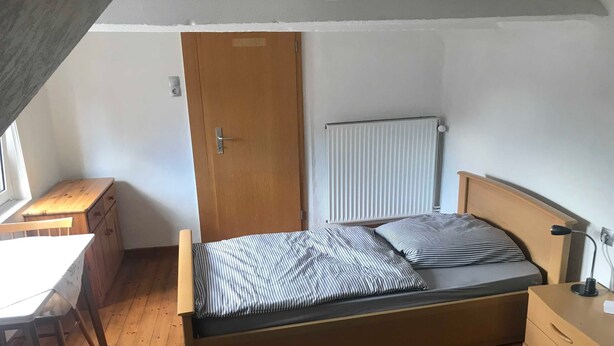 A bedroom with a wooden bed, a radiator, a wooden dresser, a desk, and a window. - Ferienhaus Villa Alwine - Ferienhaus (Börßum)