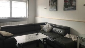 A modern living room with a leather sofa, a glass coffee table, and two framed cityscape paintings on the wall. - Ferienhaus Villa Alwine - Ferienhaus (Börßum)