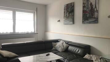 Un salon moderne avec un canapé en cuir, une table basse en verre et deux tableaux représentant des paysages urbains, encadrés et accrochés au mur.
