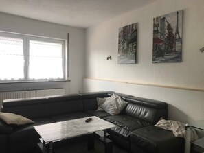 A modern living room with a leather sofa, a glass coffee table, and two framed cityscape paintings on the wall. - Ferienhaus Villa Alwine - Ferienhaus (Börßum)