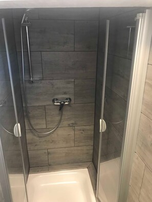 A shower with a glass door, a handheld showerhead, and a control knob.