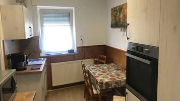 Een compacte keuken met een eettafel, een koffiezetapparaat, een oven en een raam met jaloezieën.