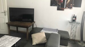 A living room with a flat-screen TV, a wooden coffee table, a grey sofa, a patterned throw pillow, and a wine rack with bottles. - Ferienhaus Villa Alwine - Ferienhaus (Börßum)