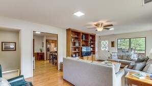 A spacious living room with a large sofa, a coffee table, and a TV. There is a bookshelf and a dining area in the background. - Beautiful Lakefront Home with Plenty of Space! (Jacksons' Gap)