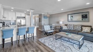 A modern kitchen with white cabinets, a stainless steel refrigerator, and a bar area with blue chairs. - Wellness Retreat - Oceanfront condo w beach access (Ponte Vedra Beach)