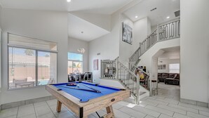 A spacious living area with a pool table, a staircase, and a view of the outdoors. - Cozy 5-Bedroom Oasis Near the Strip: Arcades, Pool, and BBQ Haven! (Las Vegas)