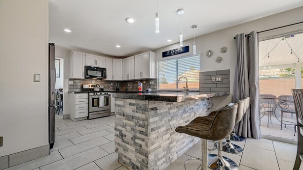 A modern kitchen with white cabinets, a granite island, and a bar area with stools. - Cozy 5-Bedroom Oasis Near the Strip: Arcades, Pool, and BBQ Haven! (Las Vegas)