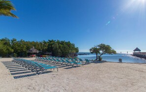 A beach with rows of sun loungers, a thatched-roof structure, and a wooden pier extending into the water.