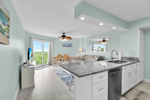 A modern kitchen with a large island, white cabinetry, and a view of greenery outside.