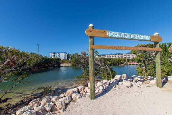 A wooden signpost with 'Ocean Pointe Marina' written on it, a sandy beach with rocks, and a body of water. - Island Getaway at Ocean Point (Tavernier)
