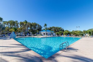 A clear blue swimming pool with a sunshade, lounge chairs, and a small pavilion.
