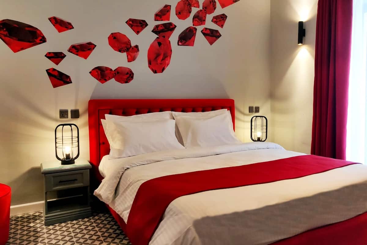 A hotel room with a red headboard, white bedding, and a geometric patterned floor.
