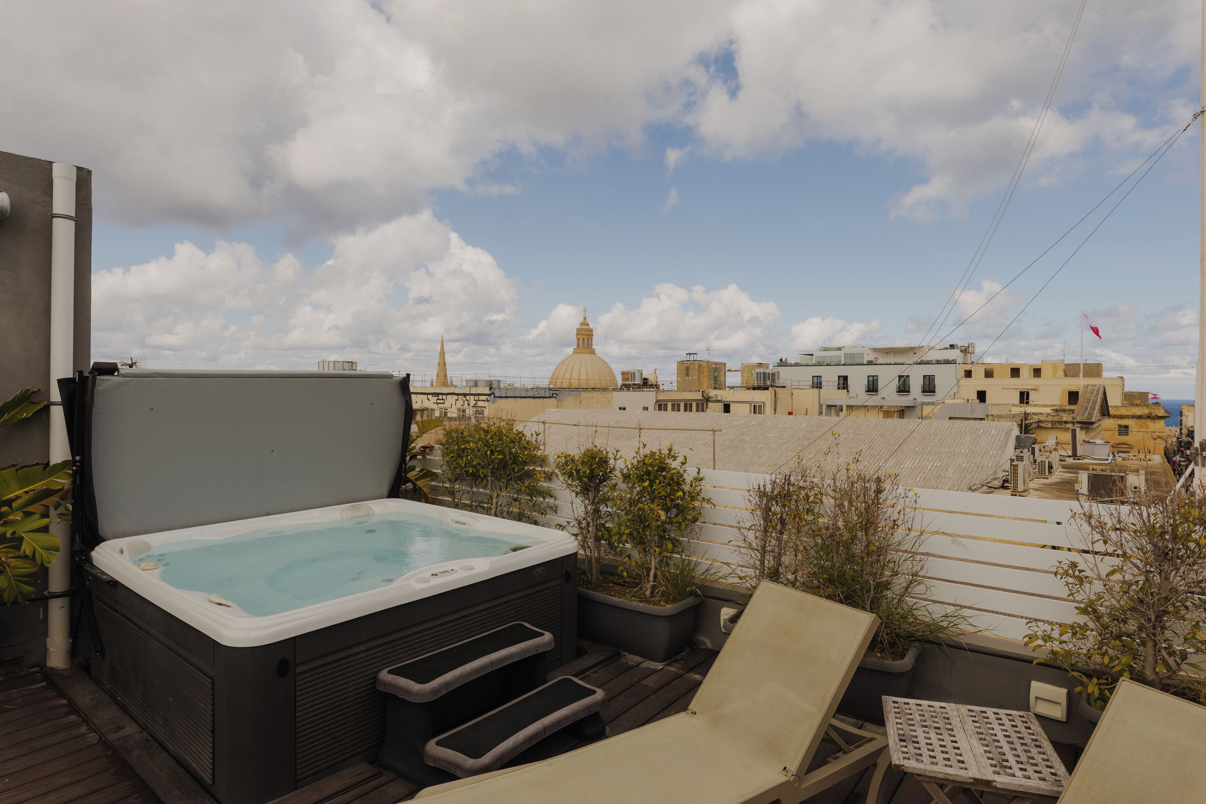 Eine Dachterrasse mit Whirlpool, Liegestühlen und Topfpflanzen.