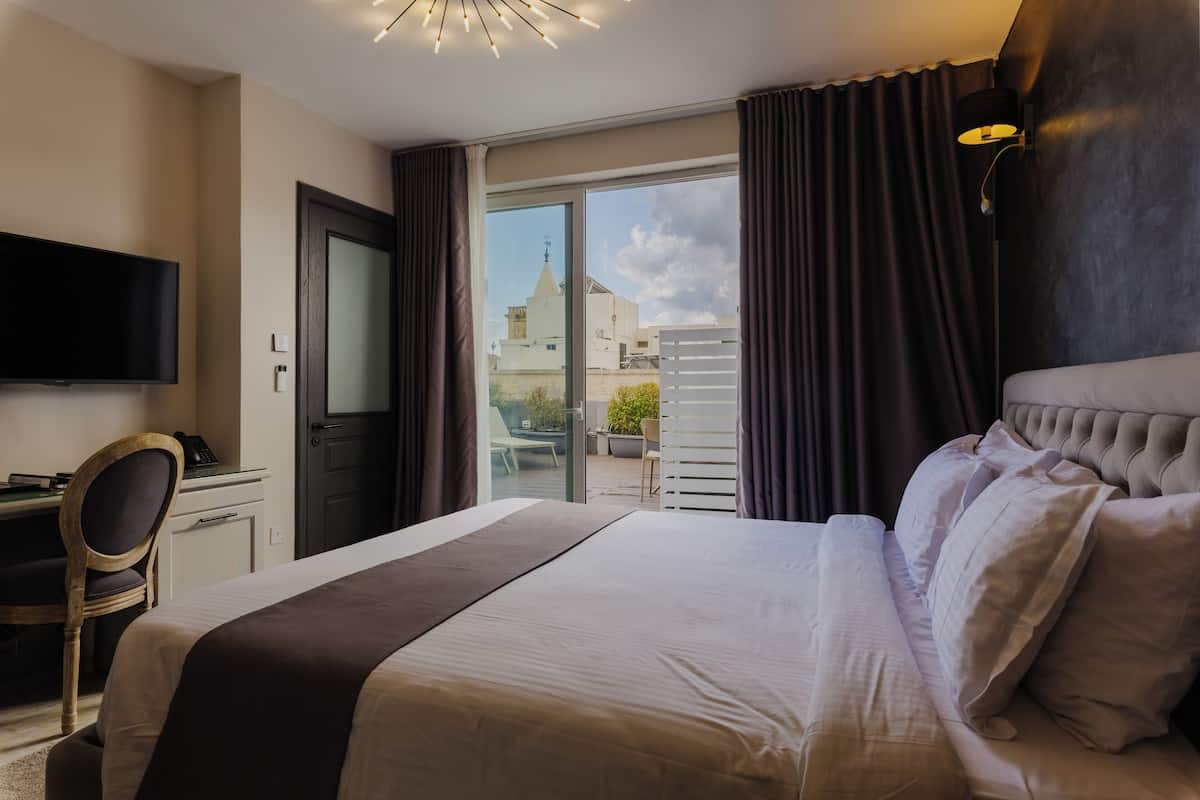 A hotel room with a large bed, a desk, a chair, a television, and a view of buildings through the window.