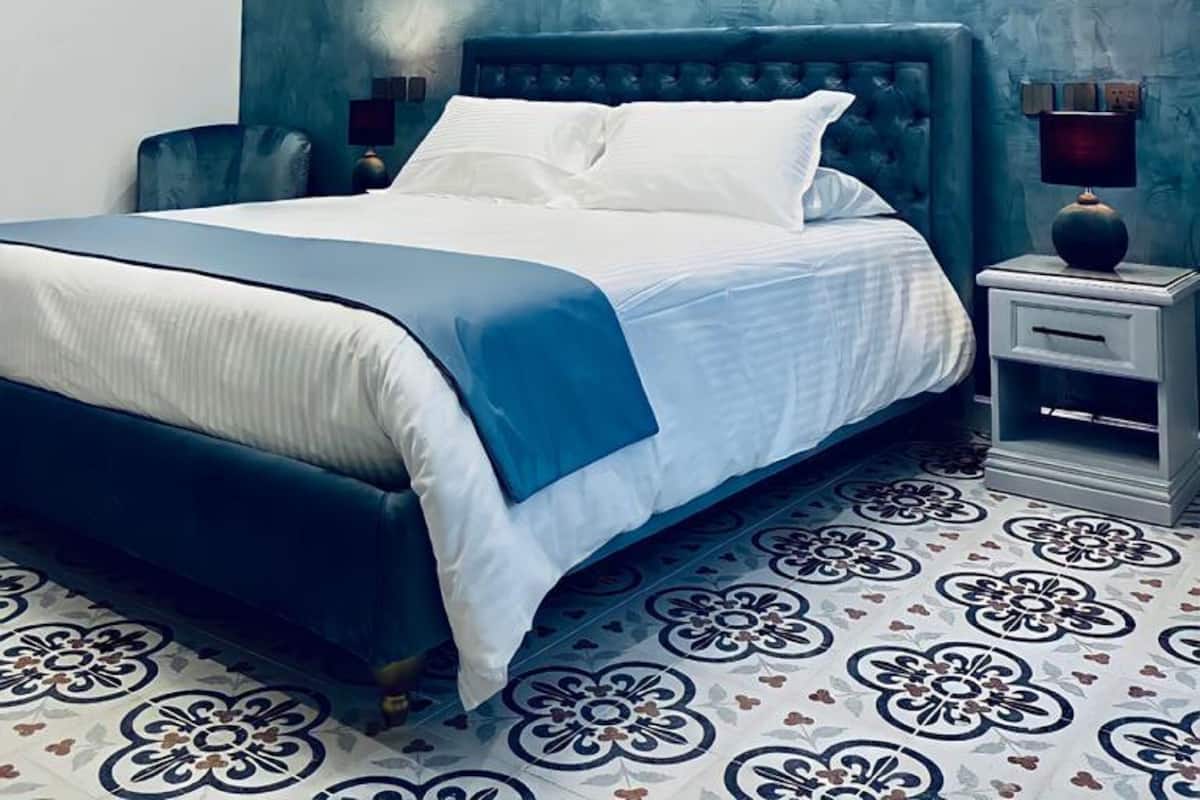 A bedroom with a bed, nightstands, a wall-mounted light fixture, and patterned floor tiles.