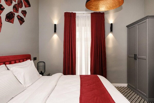 Una habitación de hotel con una cama, cortinas rojas, un armario y luces fijadas a la pared.
