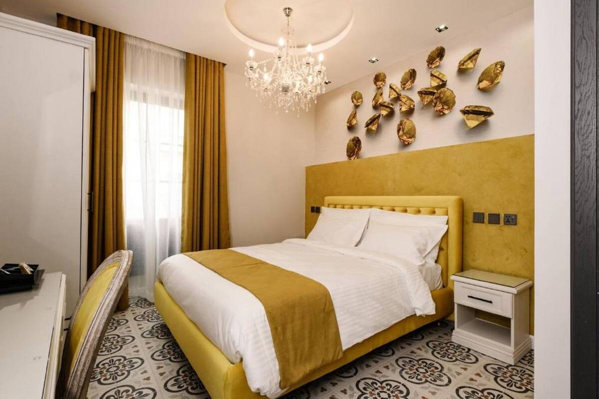 A hotel room with a bed, a bedside table, a mirror, and a chandelier.