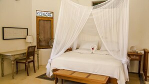 A bedroom with a four-poster bed, a wooden desk, a chair, and a bedside table with a lamp.