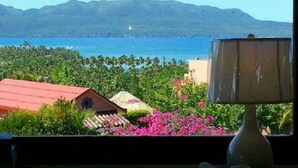 A view of a coastal area with a mountain range in the background, a red-roofed building, and a lamp in the foreground.