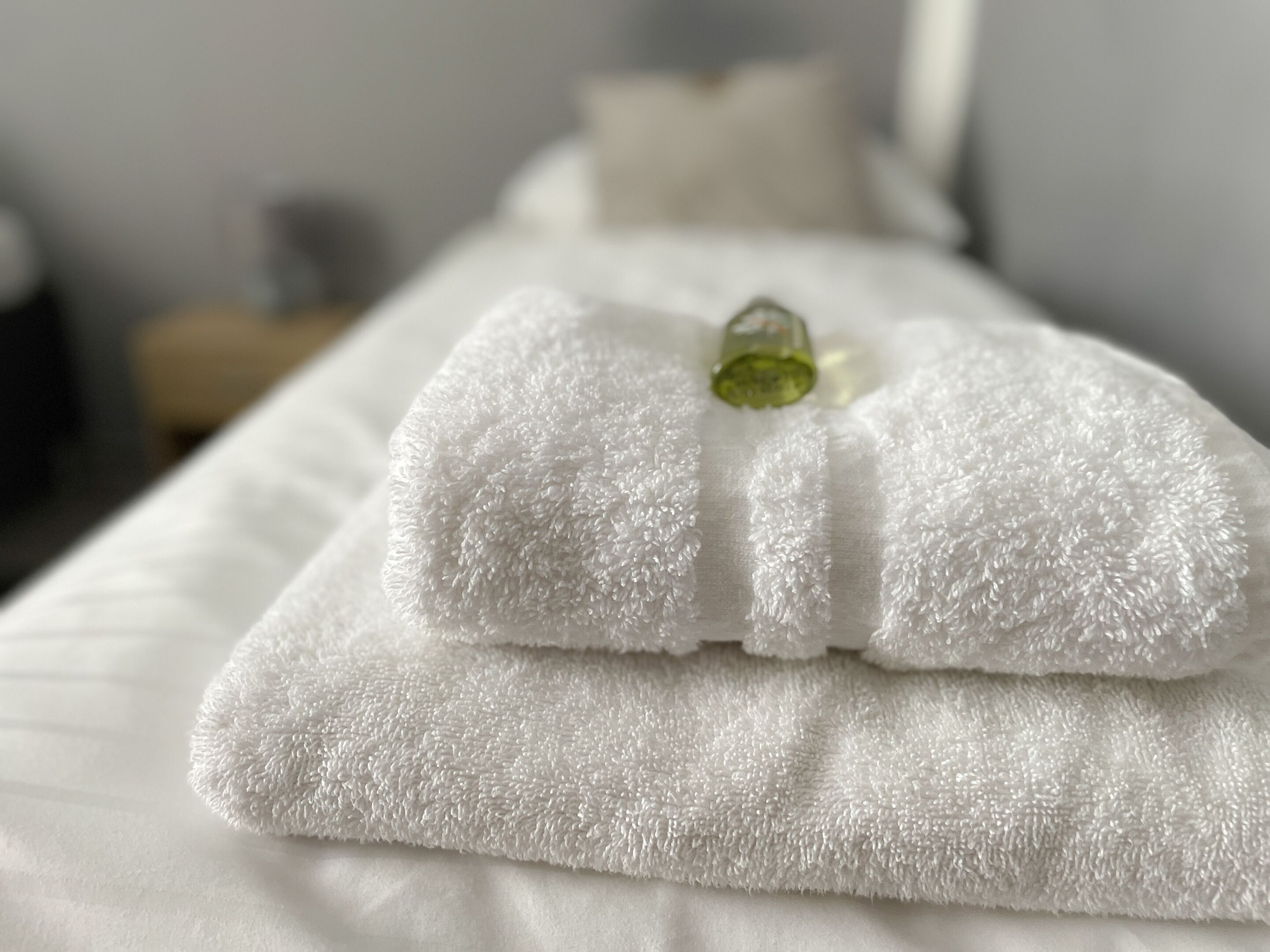 Una cama bien hecha con una toalla blanca doblada y una pequeña botella de loción encima.