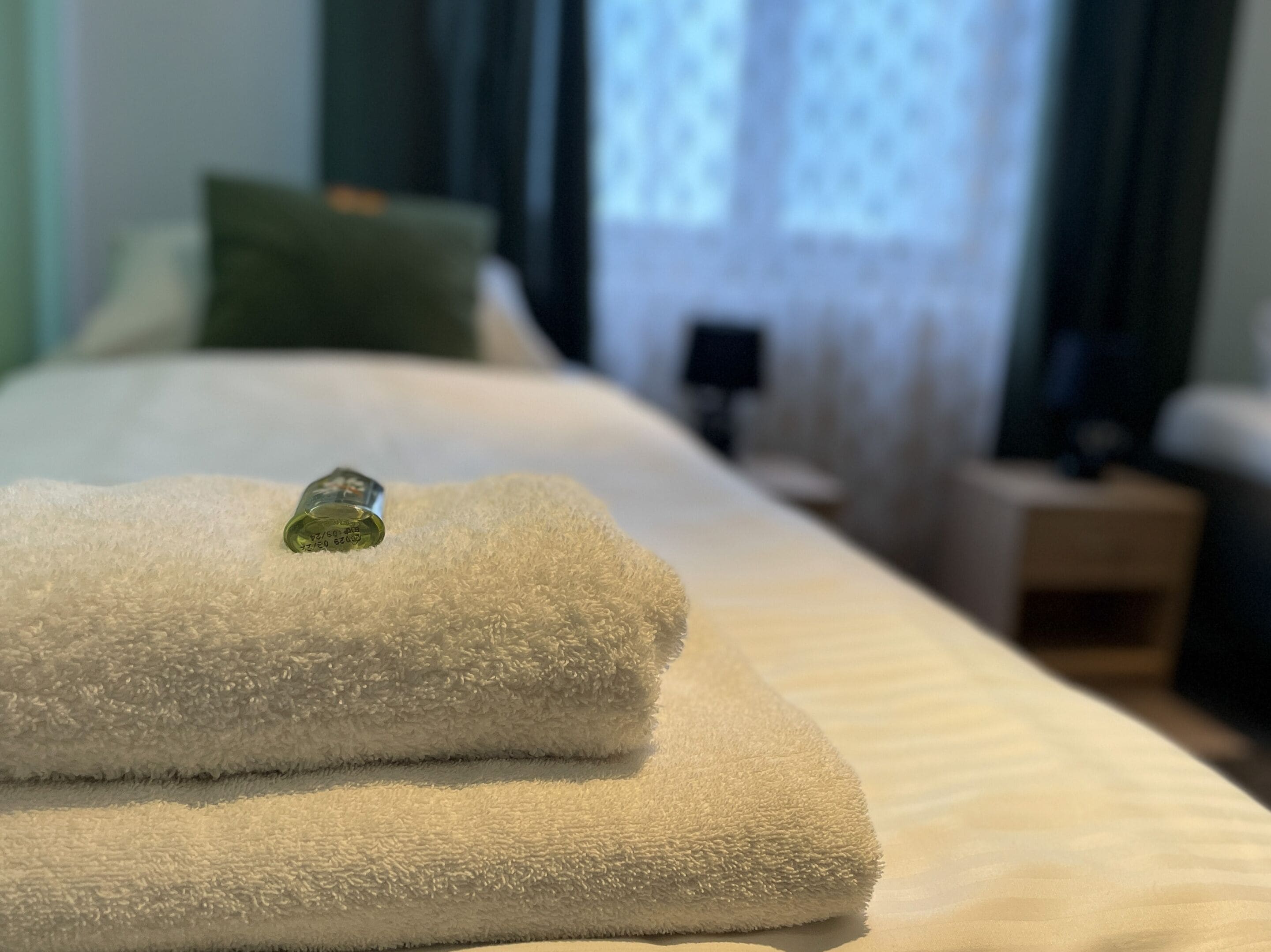 Ein ordentlich bezogenes Bett mit weißen Handtüchern und einem grünen Dekorationselement darauf.