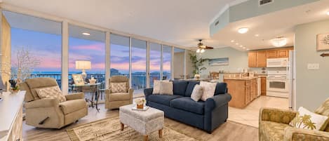 A spacious living area with a large window, a blue sofa, a beige armchair, and a patterned rug.