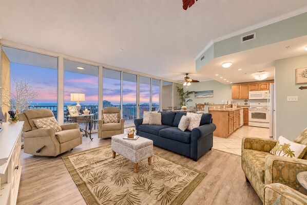 A spacious living area with a large window, a blue sofa, a beige armchair, and a patterned rug.