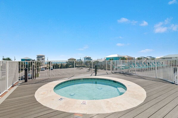 A circular hot tub on a wooden deck with a pool in the background.