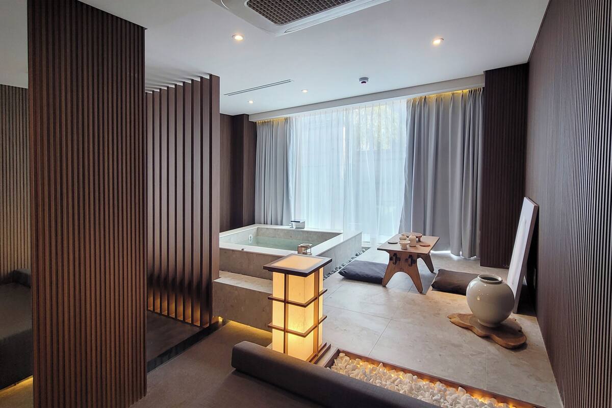 A modern bathroom with a large bathtub, a wooden partition, and a small table with a vase.