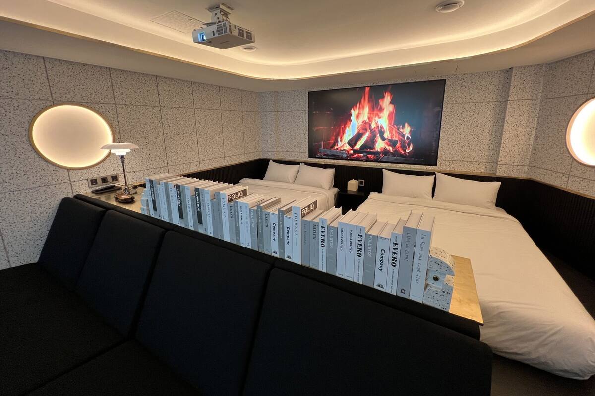 A modern hotel room with a large bed, a flat-screen TV mounted on the wall, a fireplace, and a collection of books on the bed.