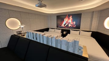 A modern hotel room with a large bed, a flat-screen TV mounted on the wall, a fireplace, and a collection of books on the bed.
