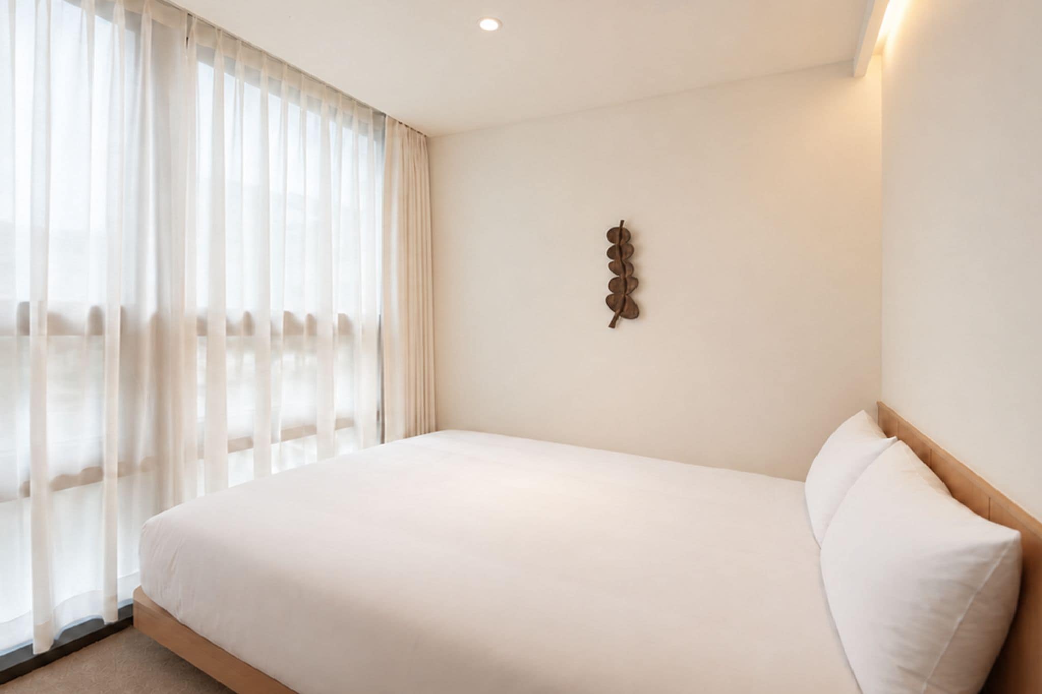 A hotel room with a large bed, a window with sheer curtains, and a wall-mounted light fixture.