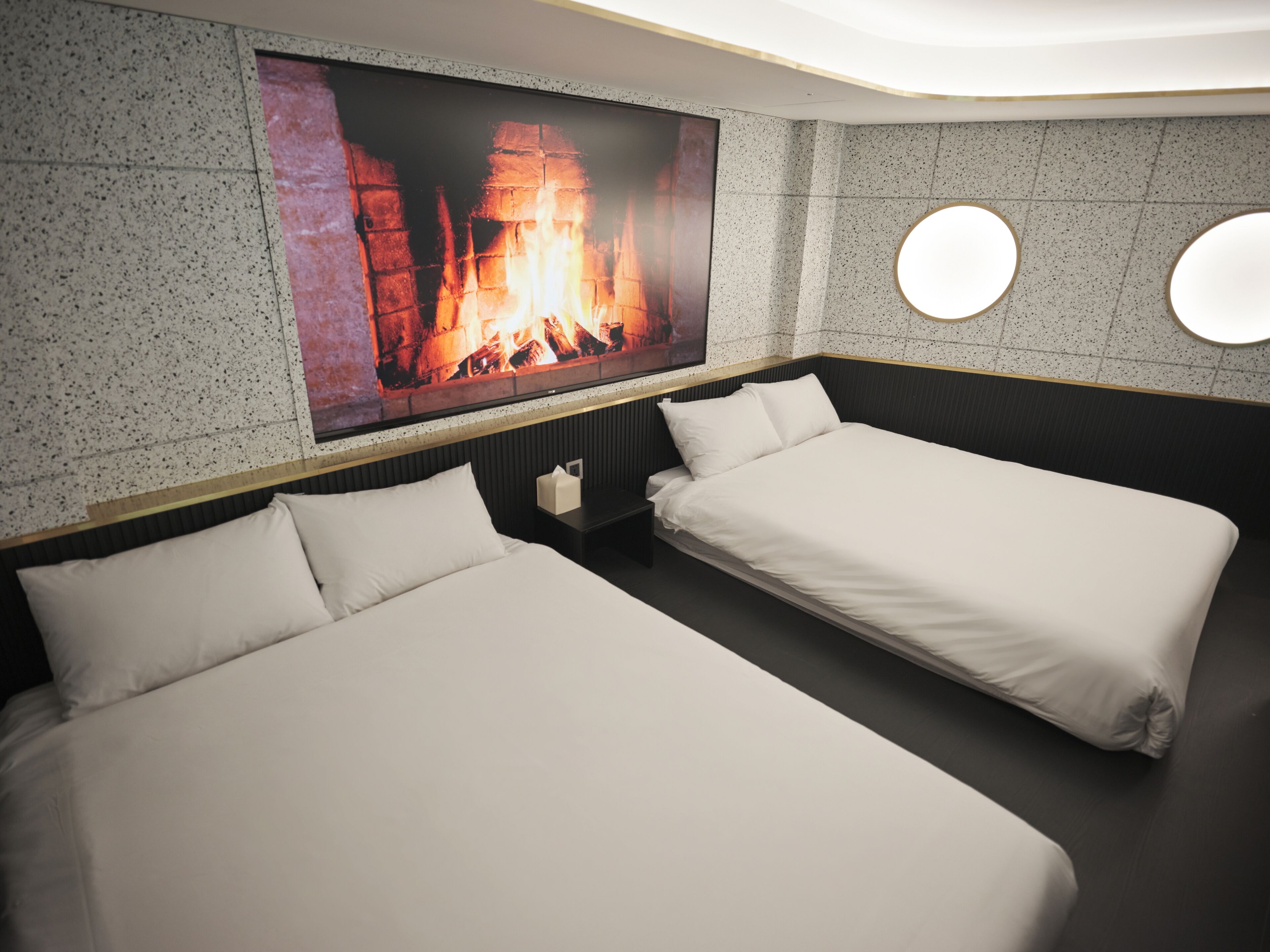 Una habitación de hotel moderna con dos camas individuales, un televisor de pantalla plana grande montado en la pared y una chimenea.