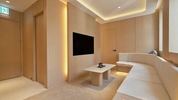 A modern, minimalist room with a flat-screen TV mounted on the wall, a small table, and a white sofa.