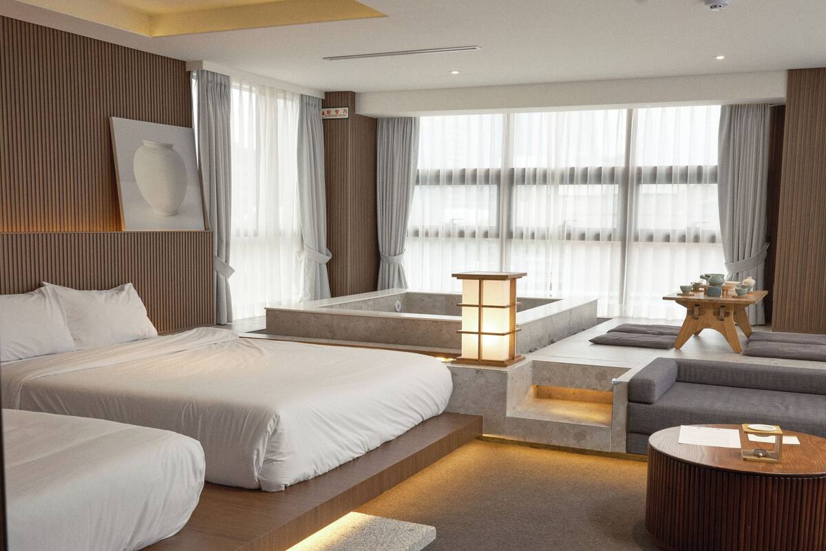 A modern hotel room with a large bed, a sofa, a coffee table, and a small table with decorative items.