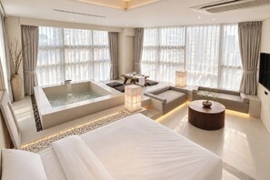 A modern hotel room with a large bed, a sitting area with a table and chairs, a bathtub, and large windows with curtains. - UH Suite The Myeongdong (Seoul)