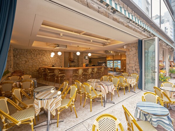 An outdoor seating area with wicker chairs and tables, a bar, and a stone wall. - UH Suite The Myeongdong (Seoul)