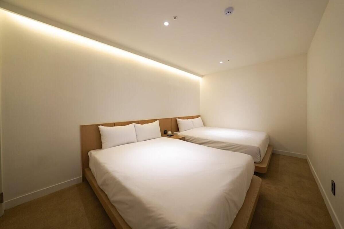 A hotel room with two beds, a wooden headboard, a small bedside table, and a carpeted floor.