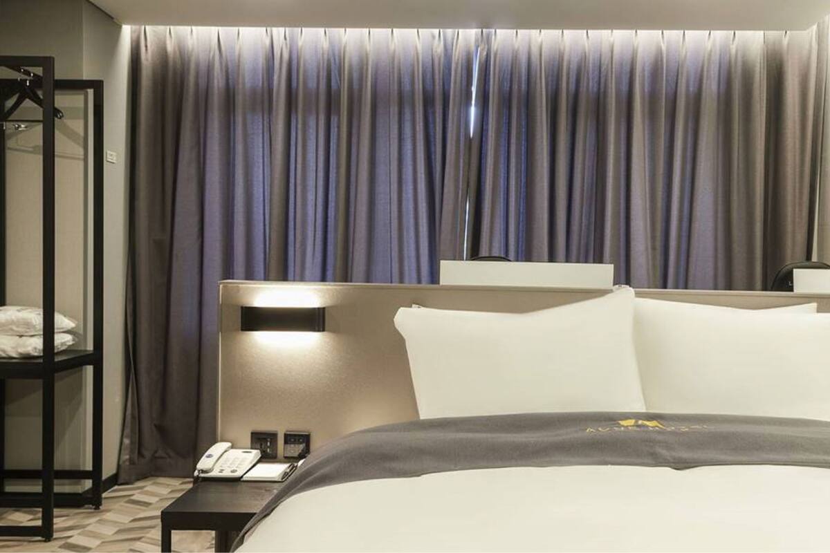 A hotel room with a large bed, a bedside table with a phone, and a wall-mounted light.