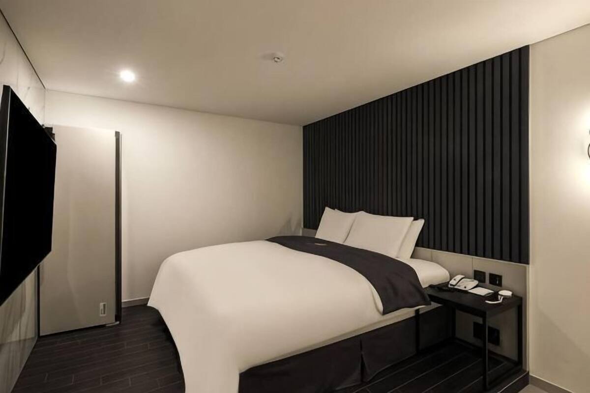 A modern hotel room with a large bed, a bedside table with a phone, a dark headboard, and a TV mounted on the wall.