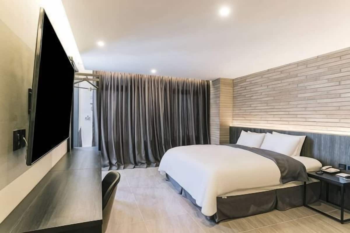A modern hotel room with a large bed, a flat-screen TV, a desk, and a nightstand.