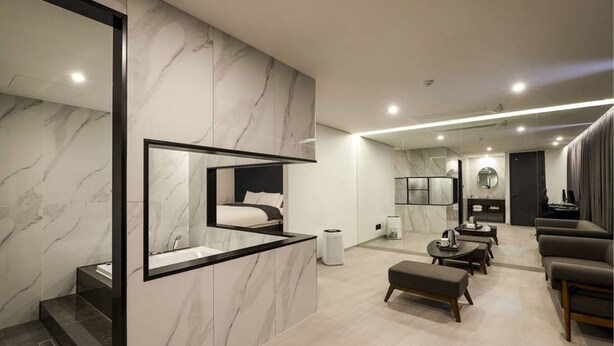 A modern hotel room with a marble wall, a large mirror, a bed, a seating area with a coffee table, and a TV. - Namyangju Aone Hotel (Namyangju)